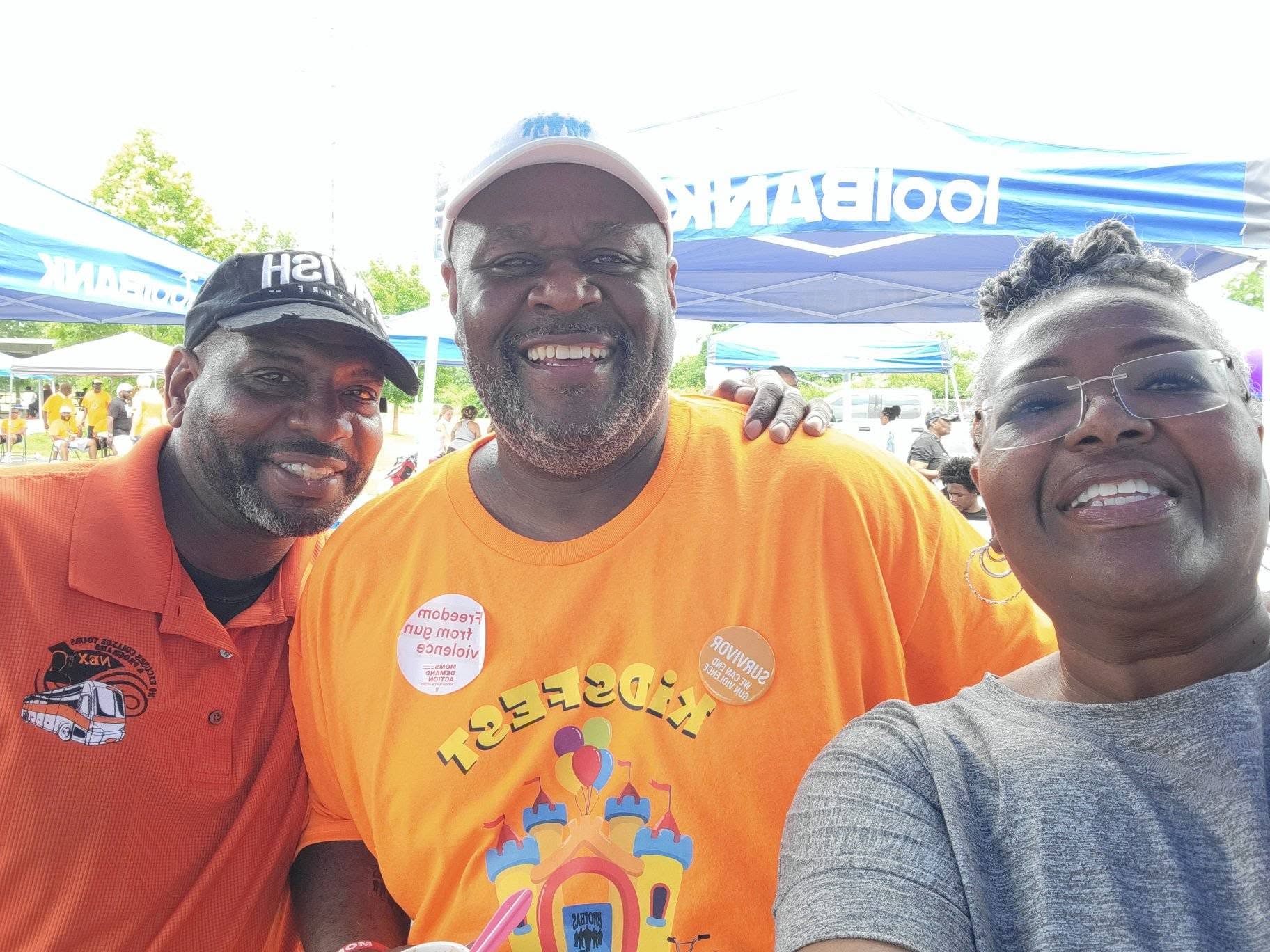 Three community leaders in orange KidsFest gear posing for a selfie