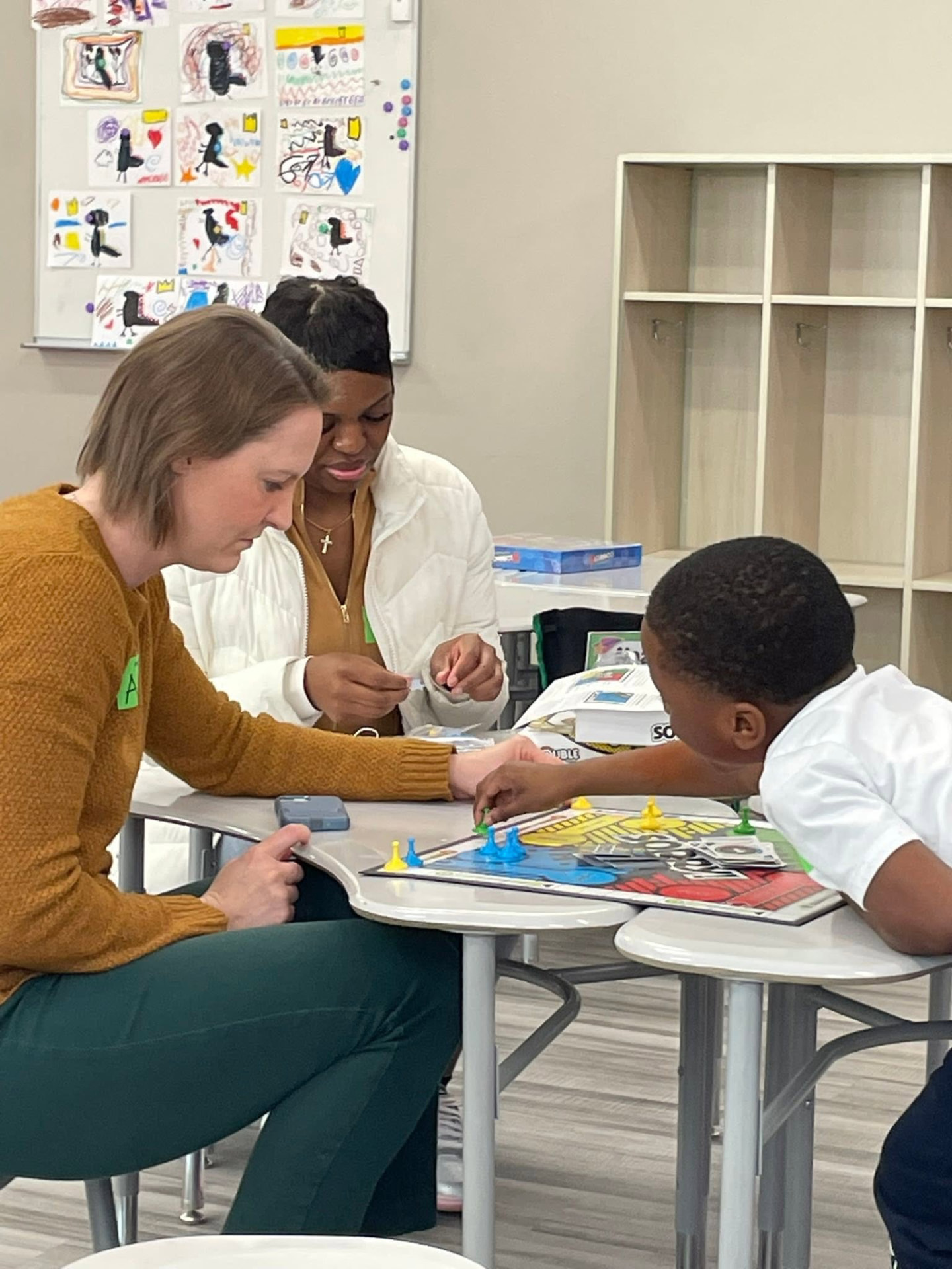 Volunteers playing a board game with a young student at the activity table