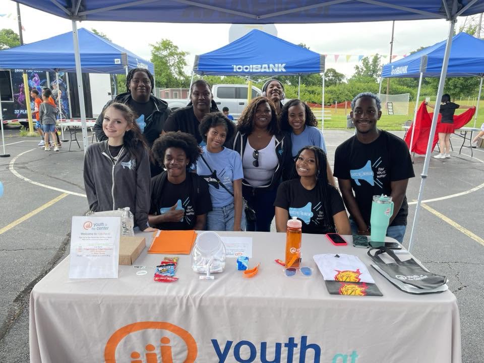 Youth At The Center team posing behind their outreach table at 3rd KidsFest