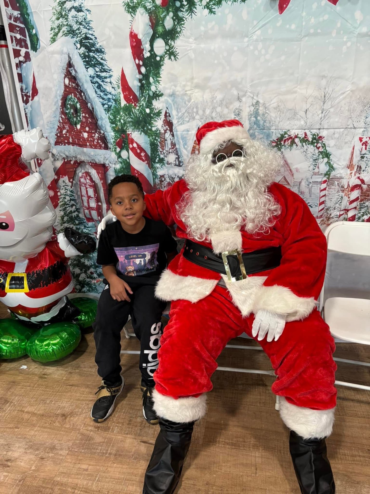 Young boy posing with Santa in front of a winter village backdrop at Brothas Inc. Jingle Jam 2025