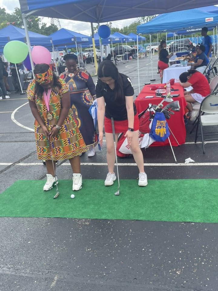 Women in African print and golf gear practicing putting at 3rd KidsFest