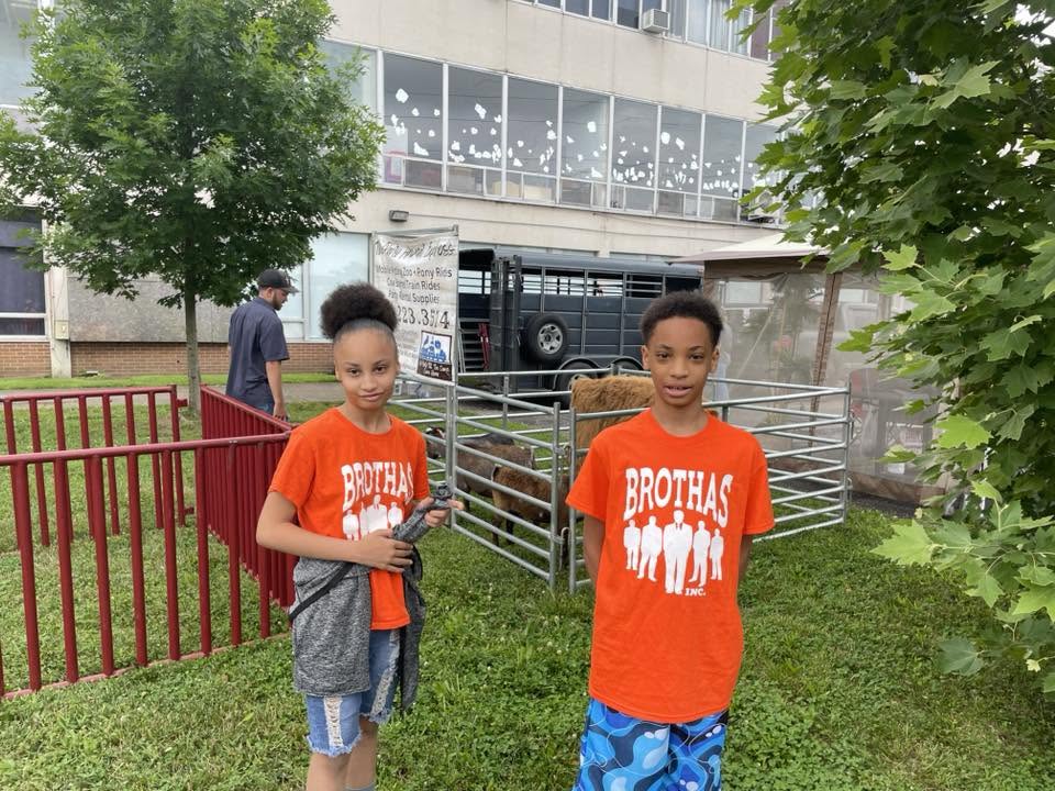 Two young students in orange Brothas Inc. shirts posing by the petting zoo at 3rd KidsFest
