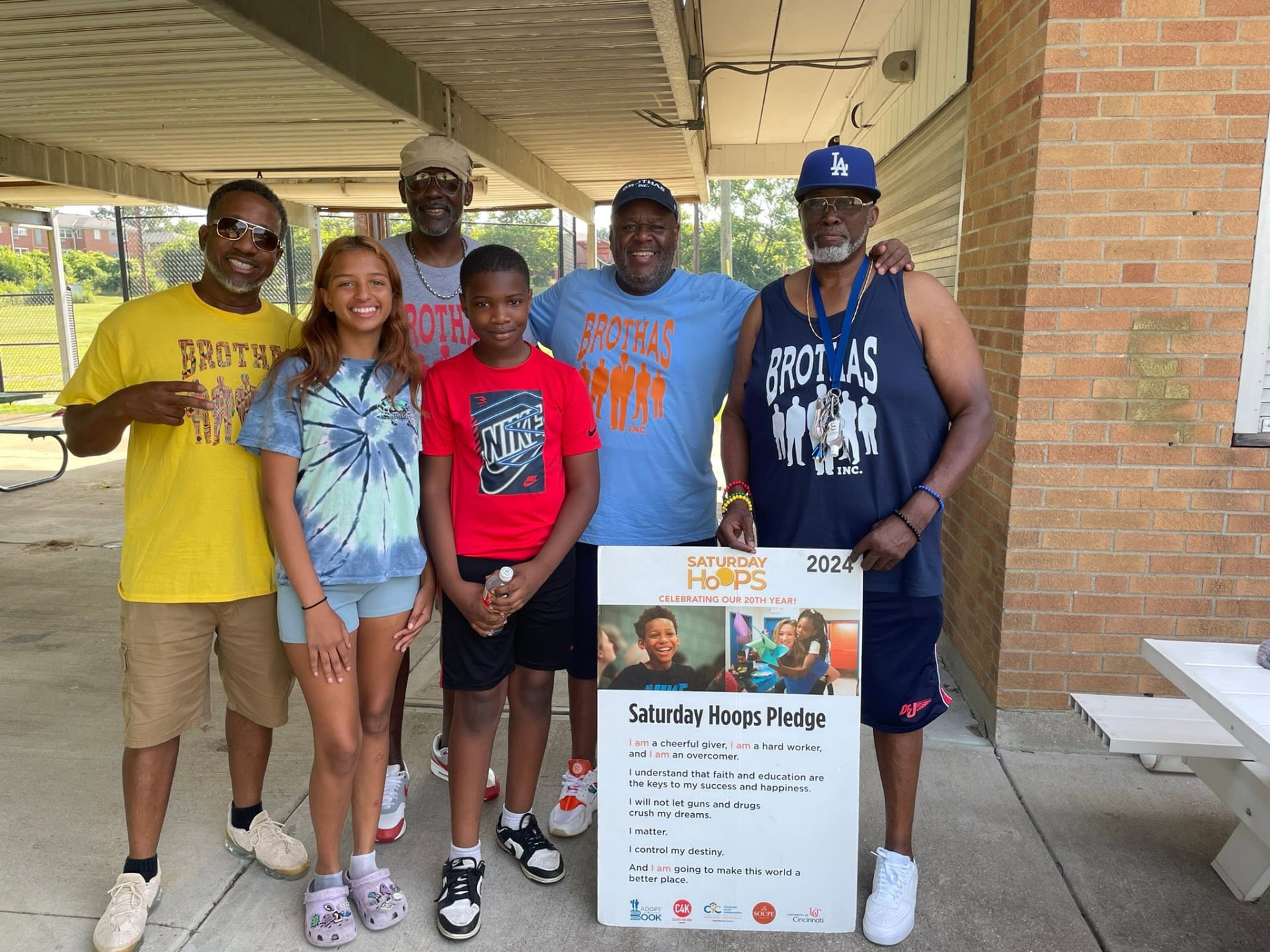 Mentors and two youth posing with the 2024 Saturday Hoops Pledge sign celebrating 20 years