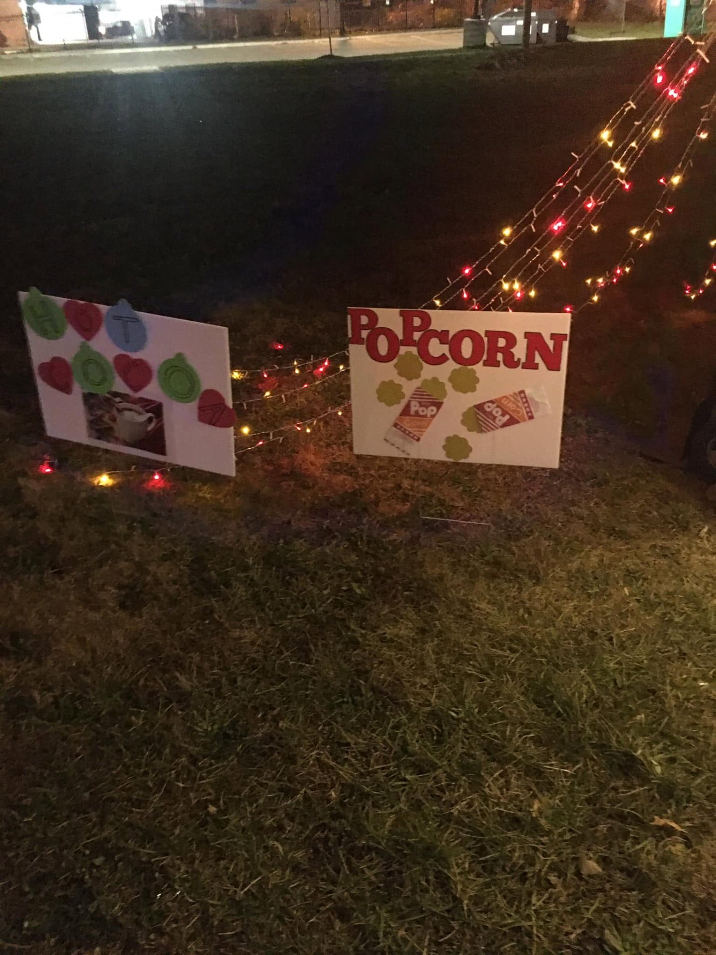 Handmade Hot Cocoa and Popcorn yard signs lit by string lights at Brothas Inc. Jingle Jam 2023