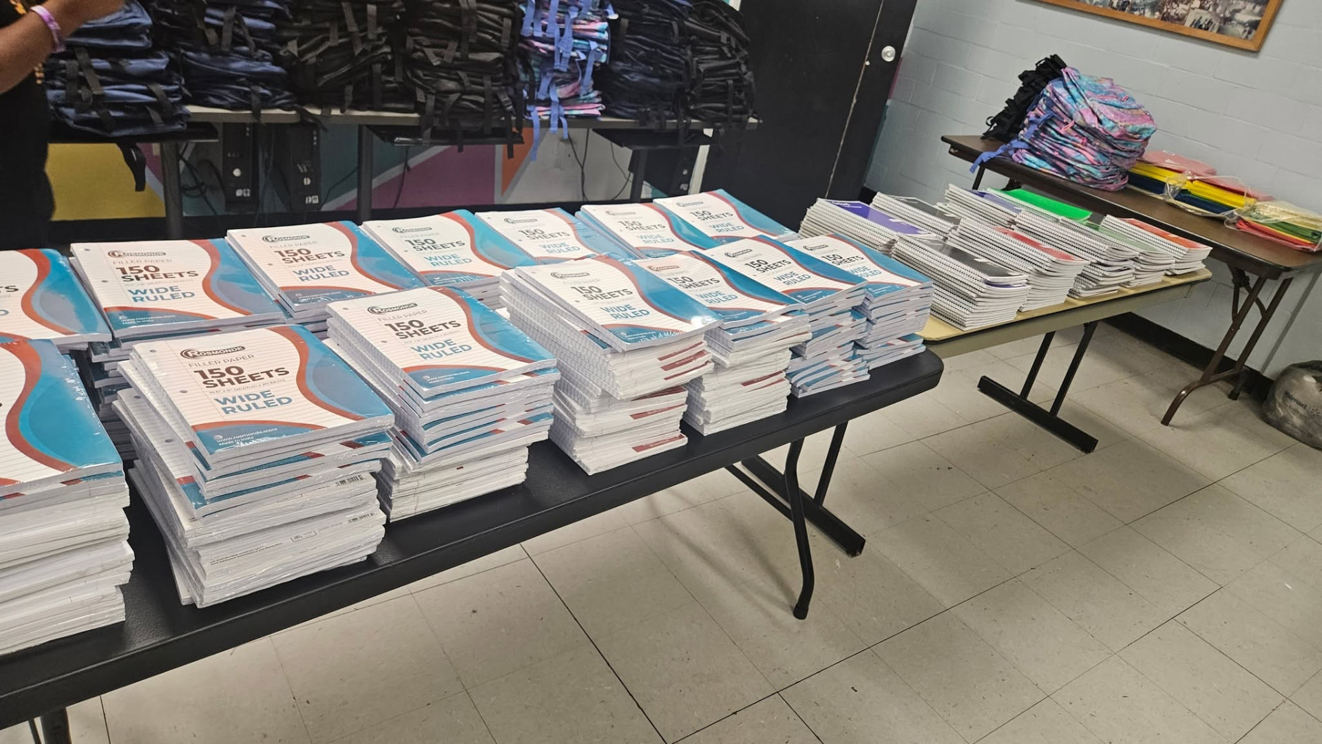 Tables of wide-ruled filler paper and notebooks prepared for the 2025 Backpack Giveaway