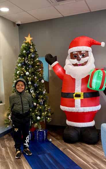 Young boy posing next to a giant inflatable Santa and lit Christmas tree at Brothas Inc. Jingle Jam 2025
