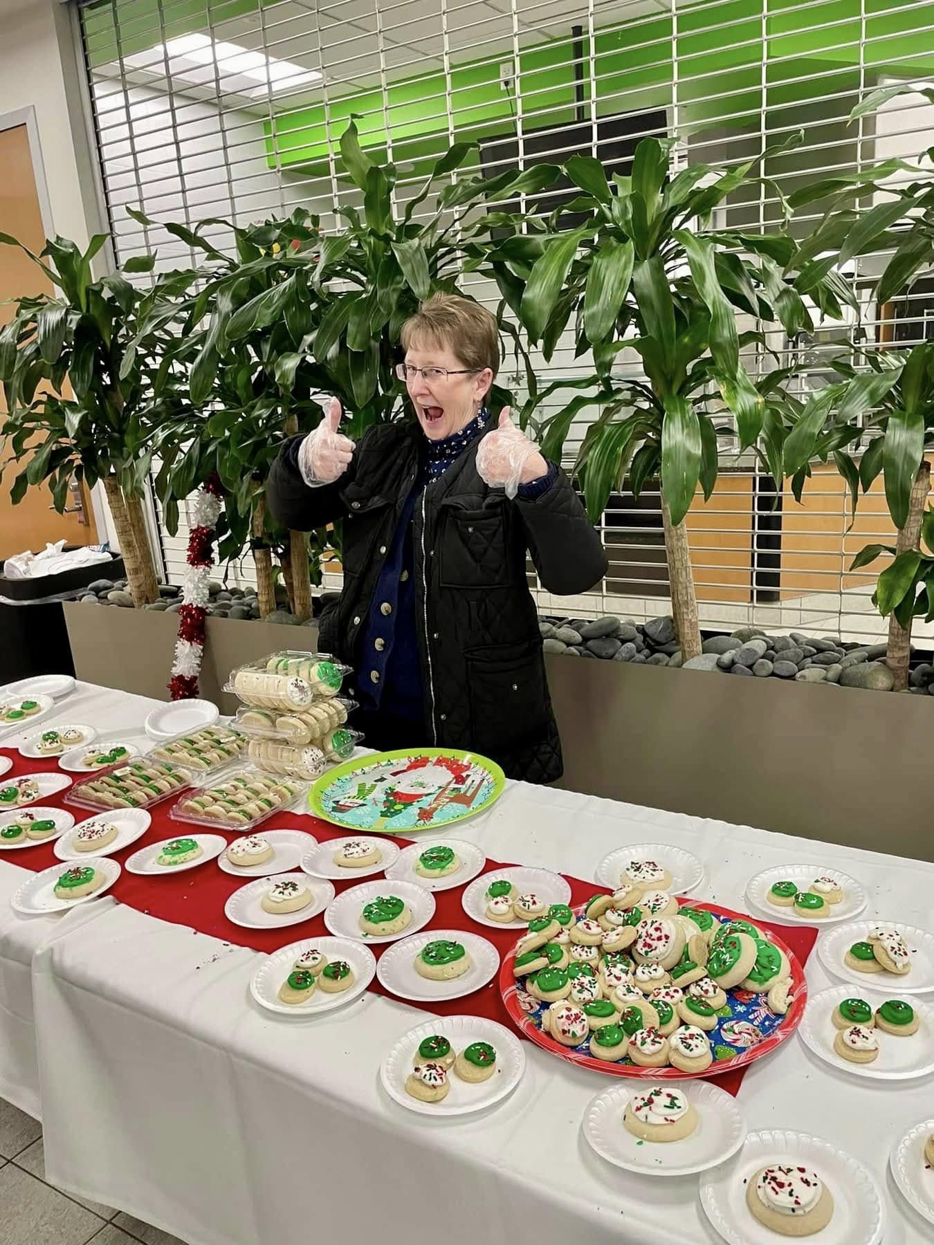 Volunteer giving a thumbs up next to trays of holiday cookies at Jingle Jam 2024