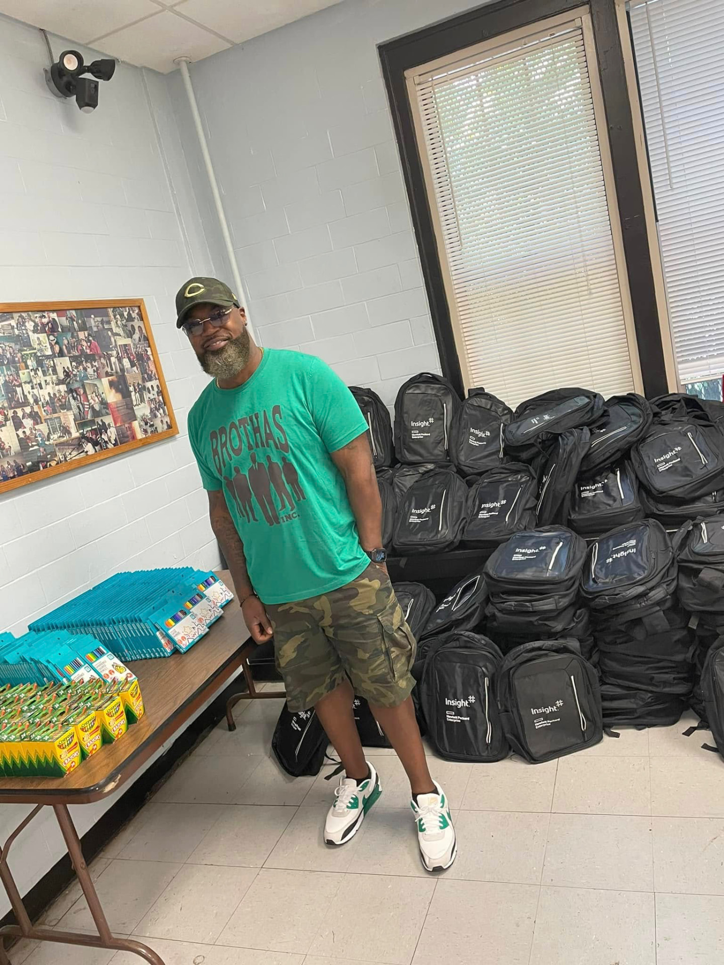 Brothas Inc. volunteer standing beside tables of crayons and markers and piles of backpacks at the 2024 Backpack Giveaway