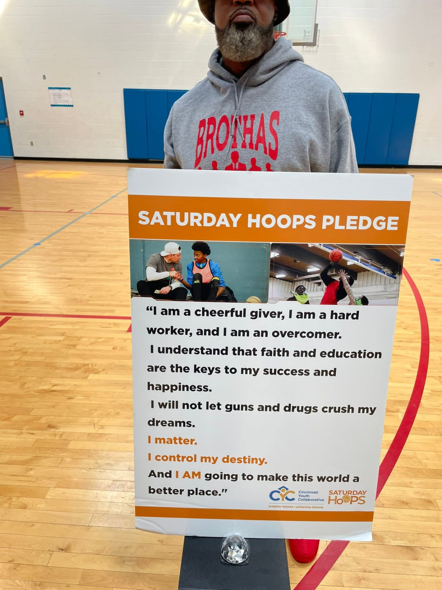 A Brothas Inc. mentor holding the Saturday Hoops Pledge sign in the gym