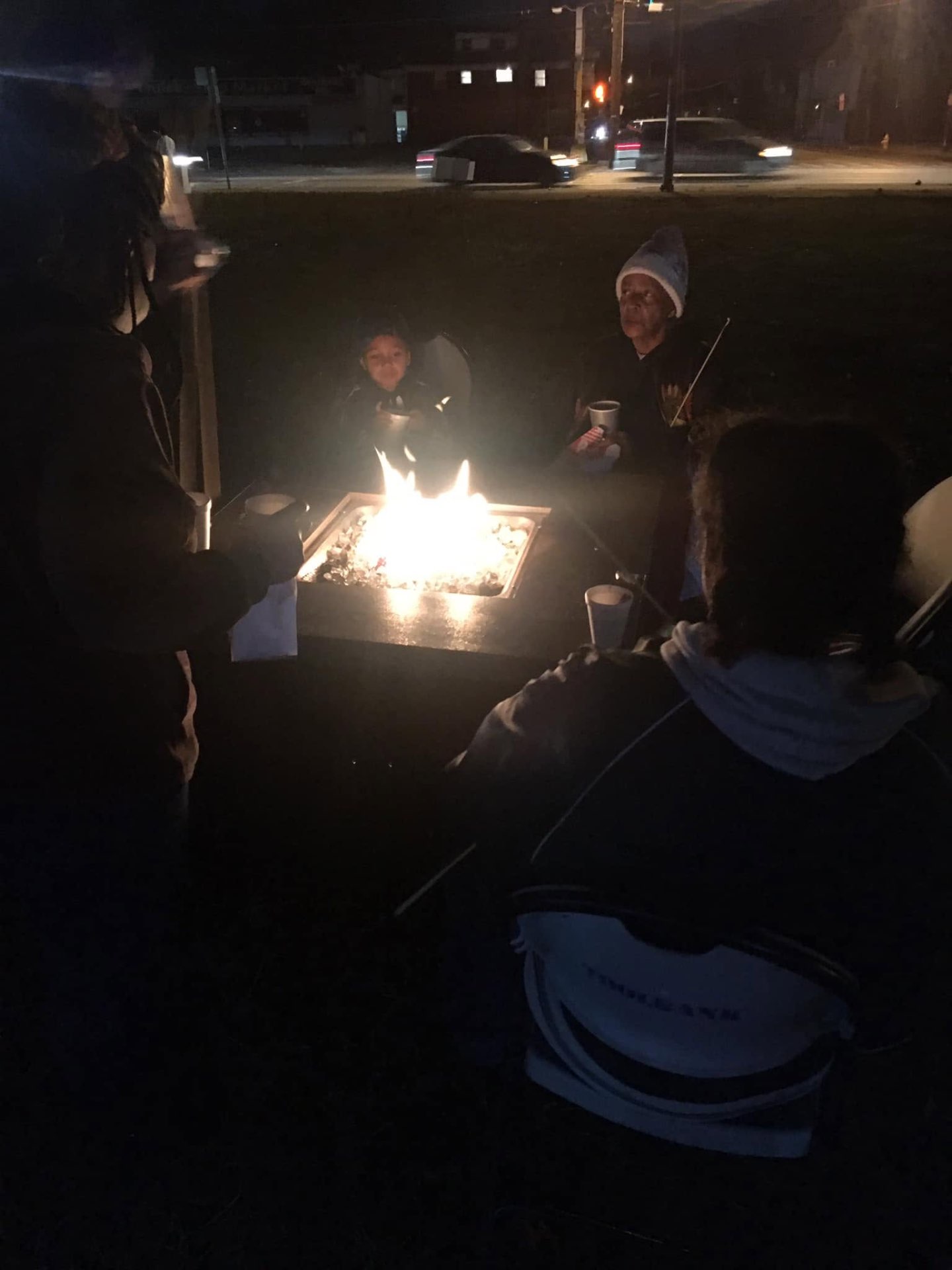 Family gathered around a glowing fire pit sharing cocoa on a cold night at Brothas Inc. Jingle Jam 2023