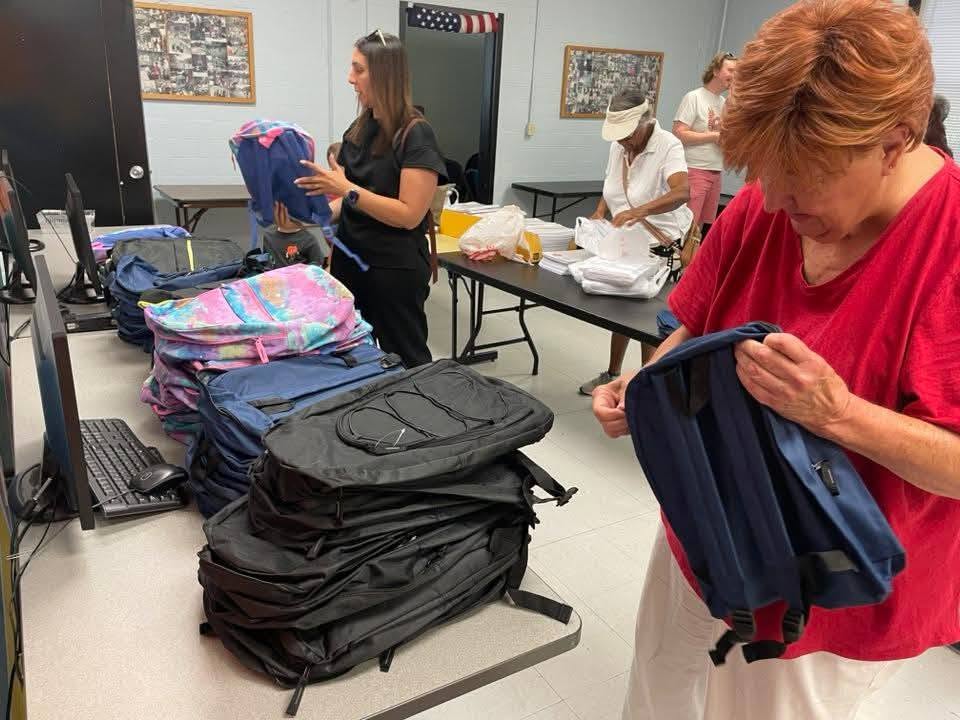 Volunteers sorting stacks of backpacks in the community room at the 2025 Backpack Giveaway