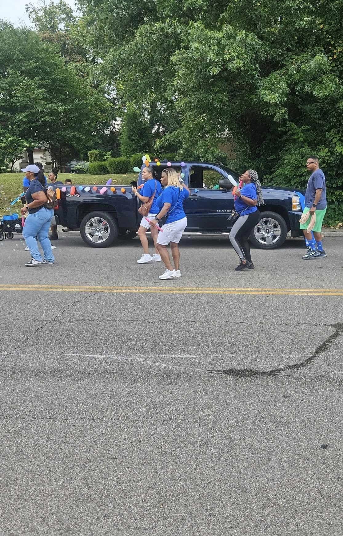 Community group in blue shirts marching alongside a decorated truck at the Black Family Reunion 2024 parade