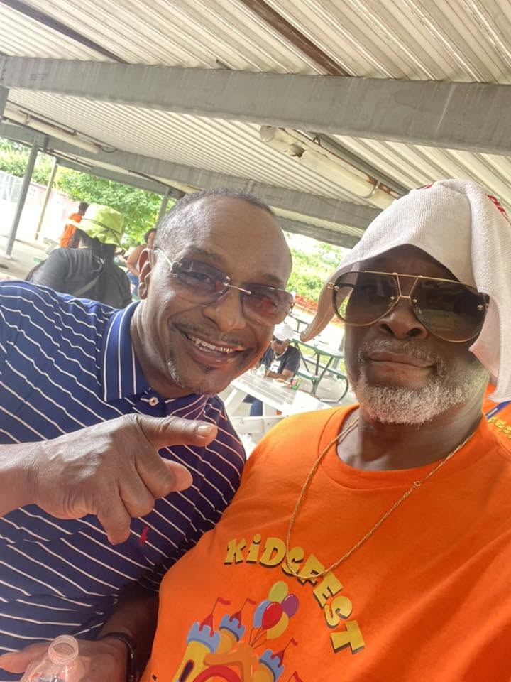 Two Brothas Inc. mentors in shades and KidsFest orange sharing a laugh under the pavilion