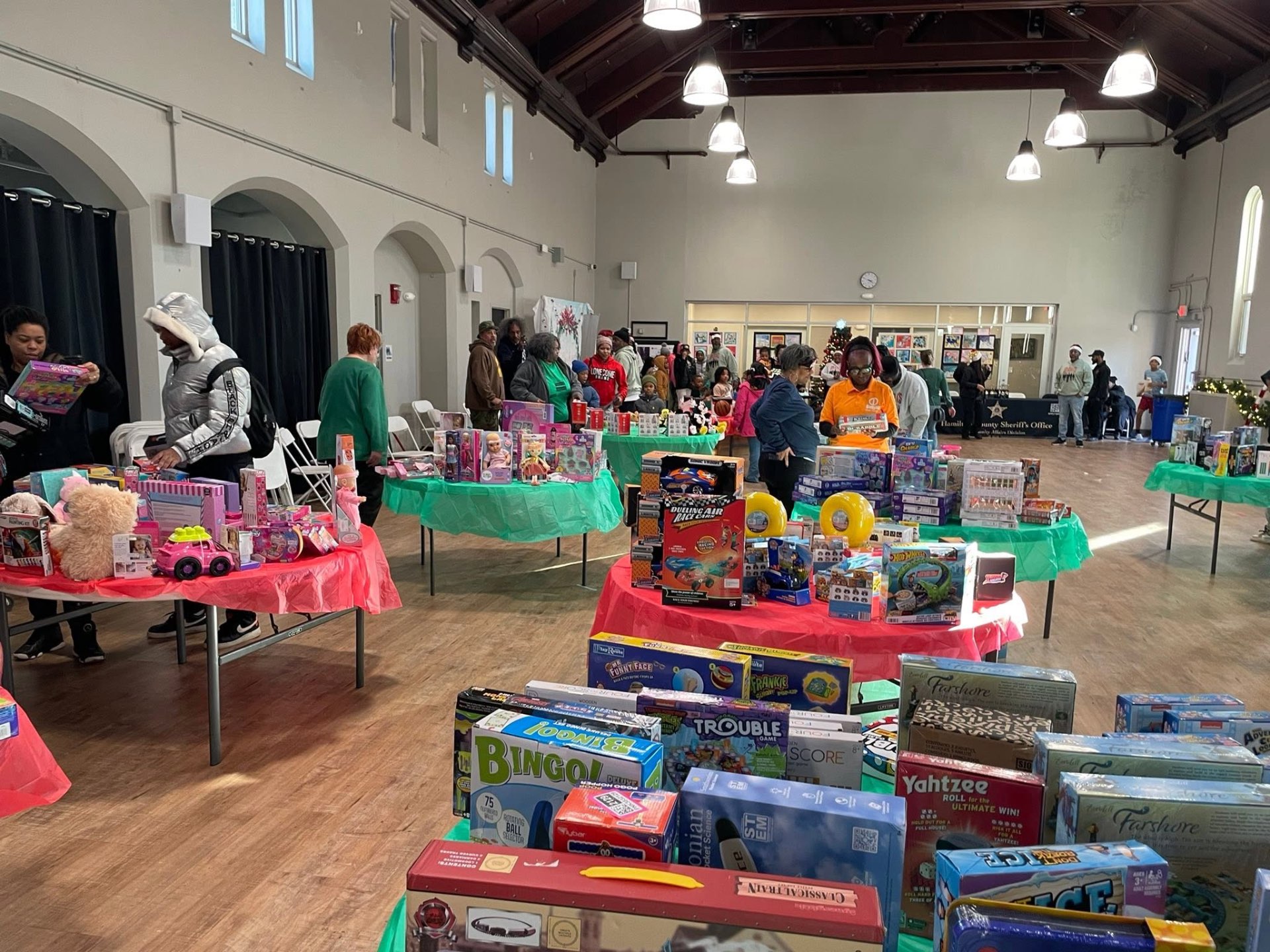 Long hall filled with tables of toys, games and gifts being selected by families at Brothas Inc. Jingle Jam 2025