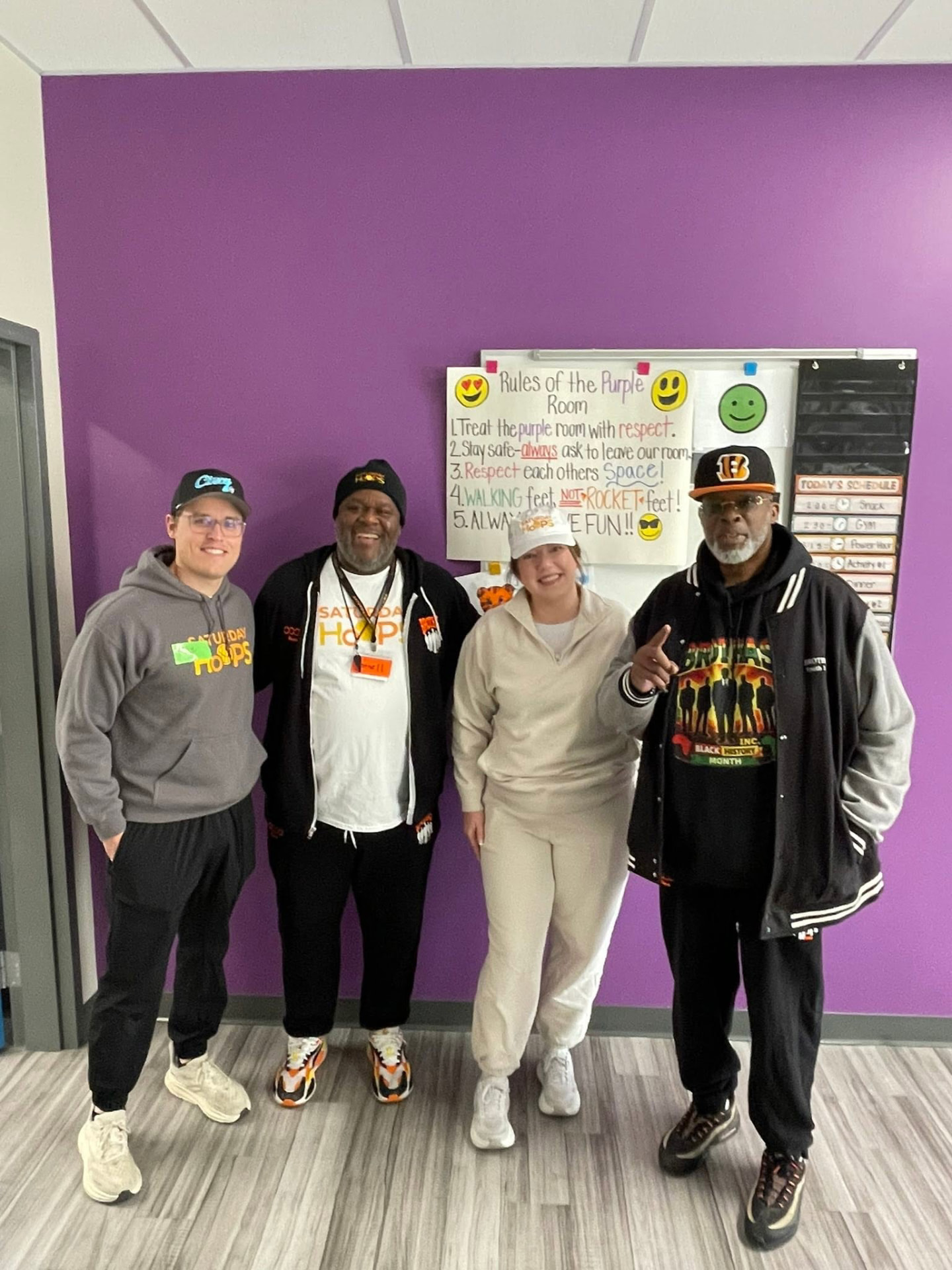 Four Saturday Hoops mentors posing in front of the purple room rules poster