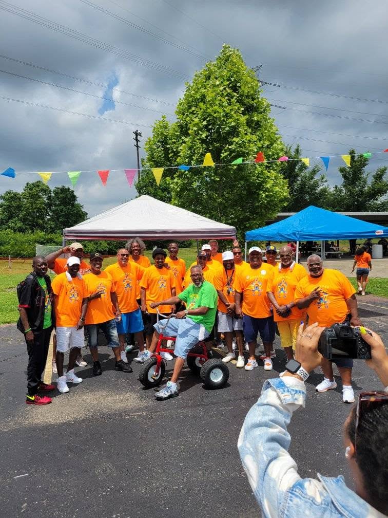 Full group photo of Brothas Inc. mentors in orange KidsFest shirts under the tent