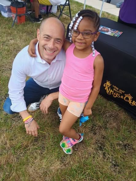 Volunteer with young girl at Save Our Youth Kings & Queens booth