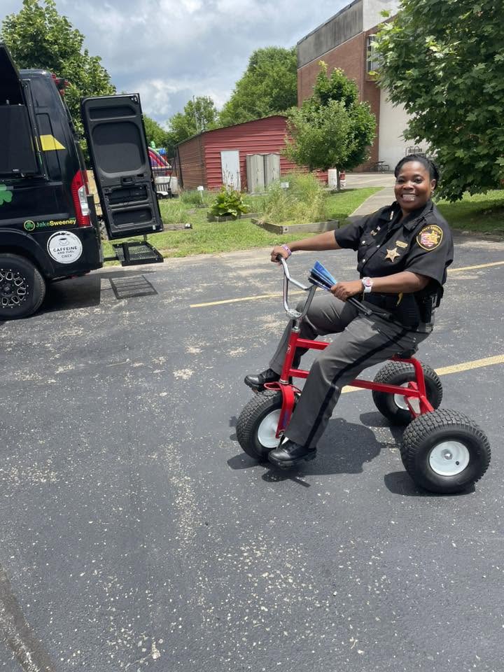 Smiling Hamilton County Sheriff deputy riding a big-wheel trike at 3rd KidsFest
