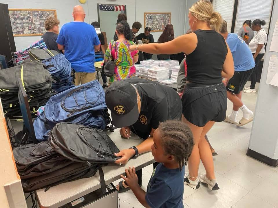 A deputy and volunteers handing backpacks to a young boy at the 2025 Backpack Giveaway