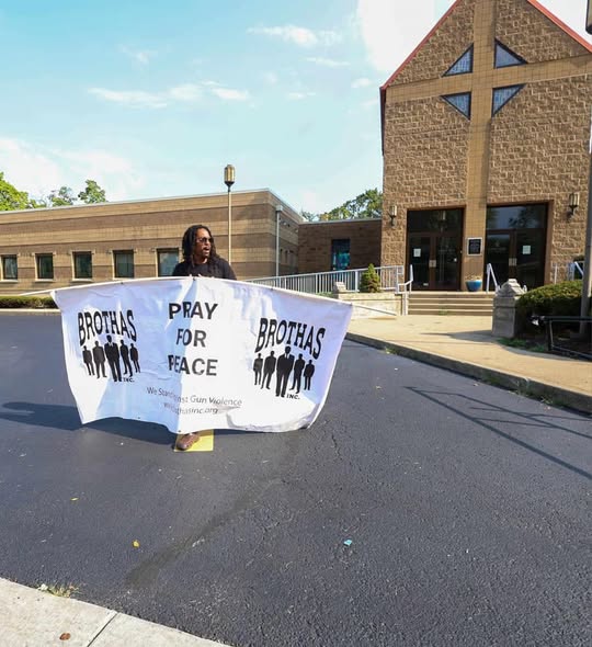 Volunteer holding a Brothas Inc. Pray For Peace banner outside a Cincinnati church at the Black Family Reunion 2024