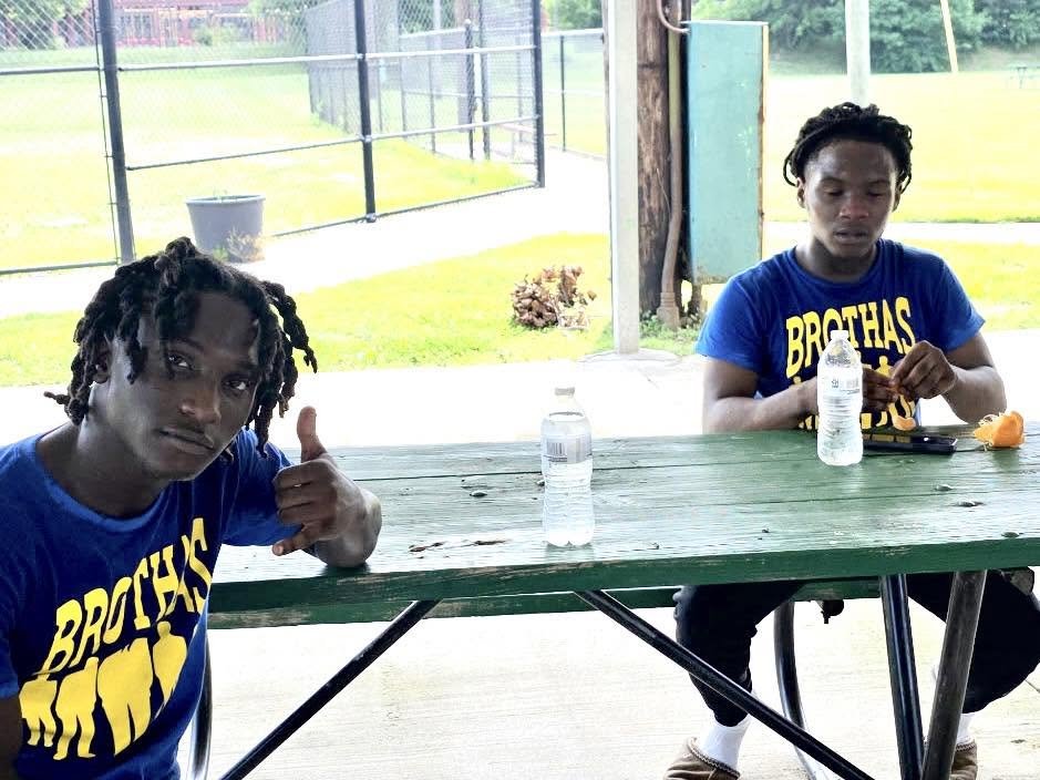 Two young men in blue and gold Brothas Inc. shirts sitting at a picnic table at Saturday Hoops