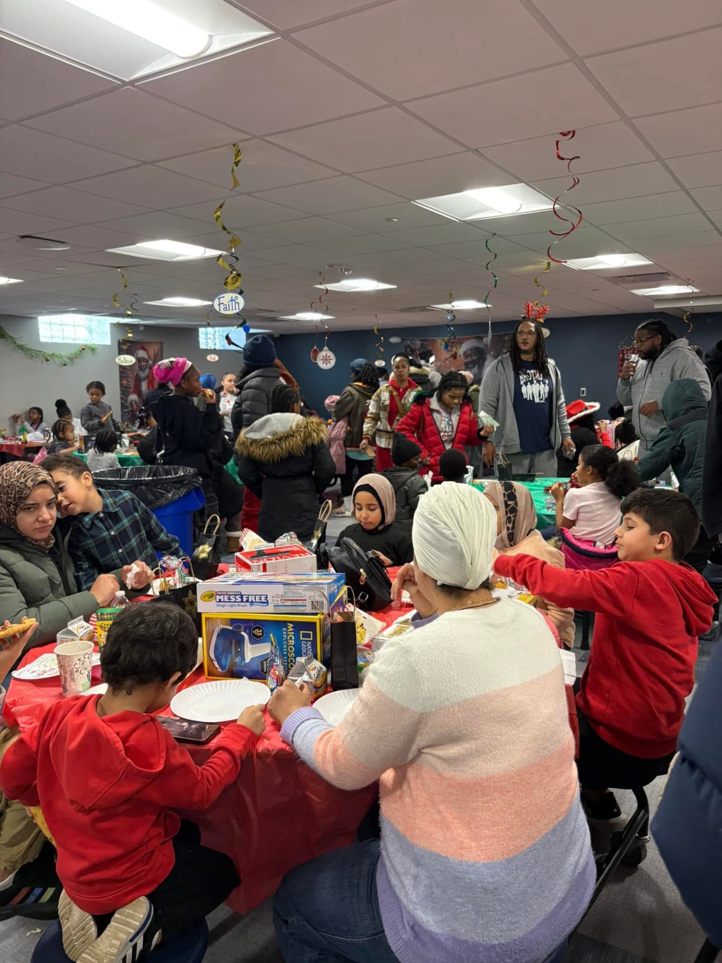 Families of many backgrounds sharing tables loaded with toys and treats at Brothas Inc. Jingle Jam 2025