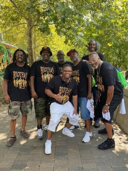 Group of Brothas Inc. mentors in kente-print shirts posing together under trees at the Black Family Reunion 2024