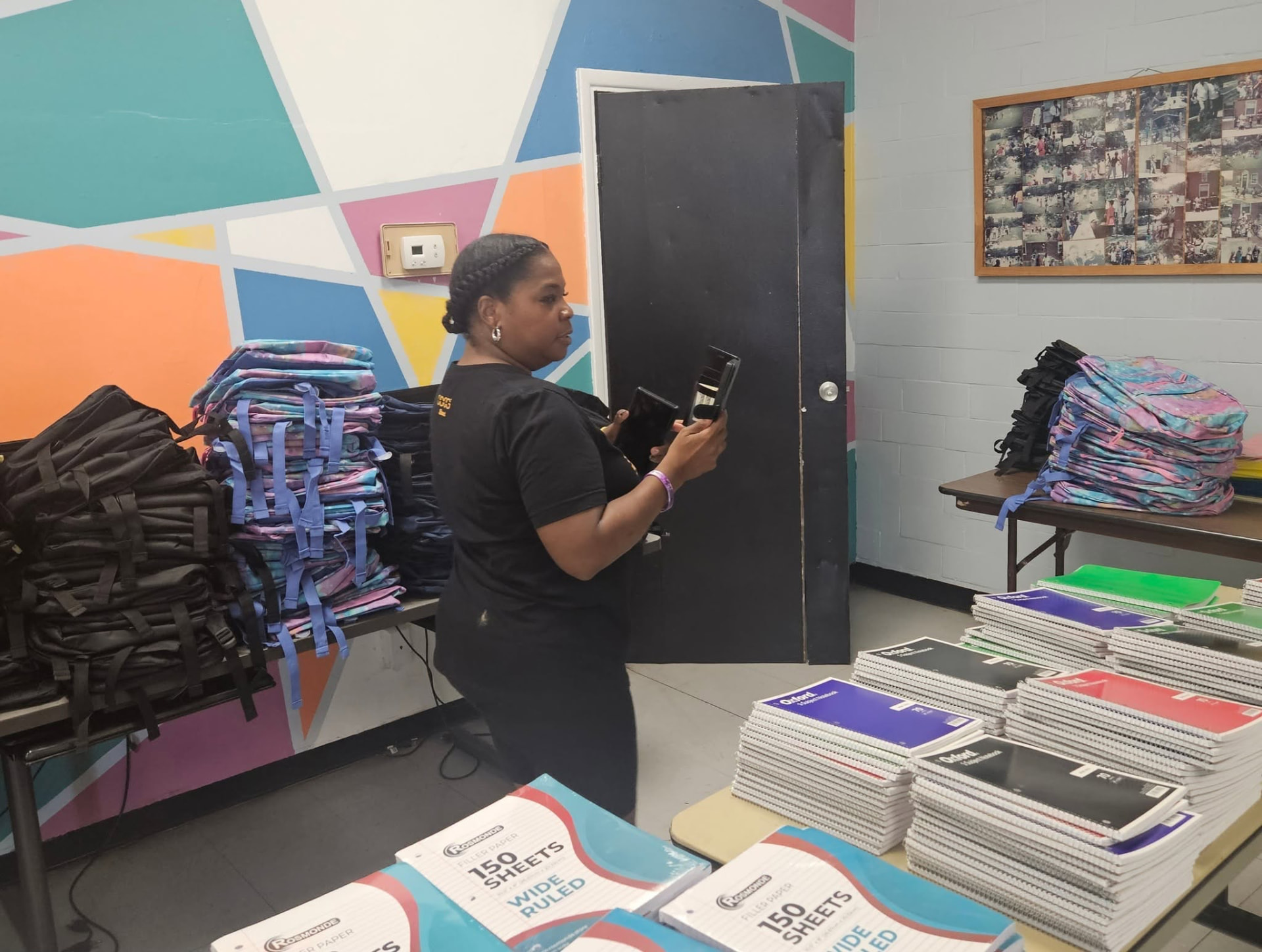 A volunteer organizing backpacks and notebooks in front of a colorful geometric mural