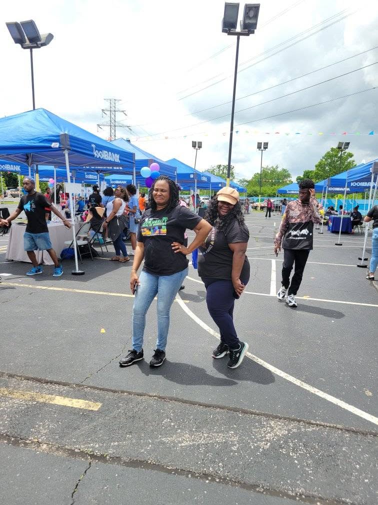 Two women posing confidently in front of the ToolBank tents at 3rd KidsFest