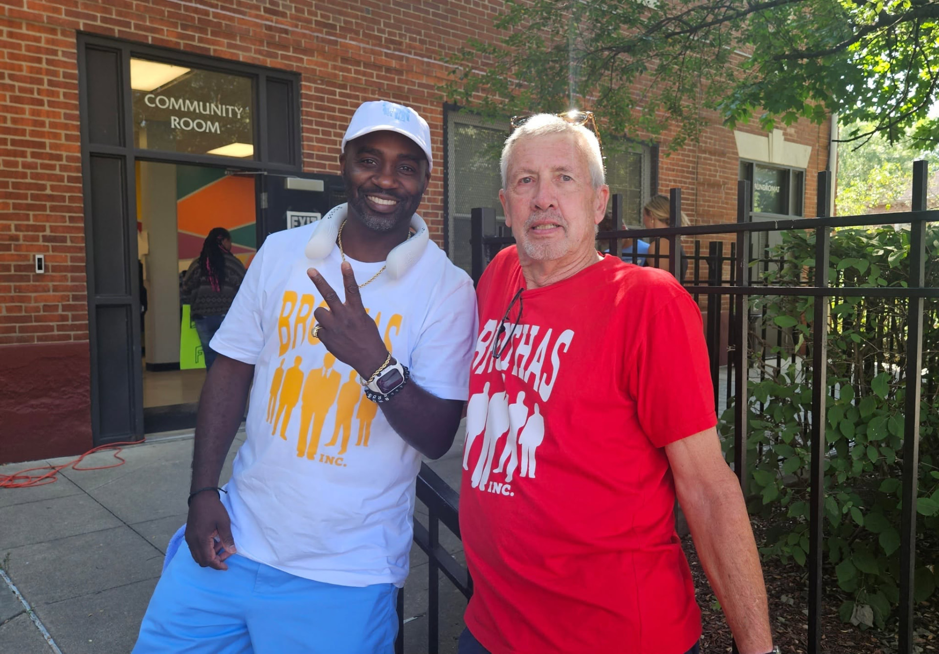 Two Brothas Inc. volunteers in branded white and red shirts posing outside the community room
