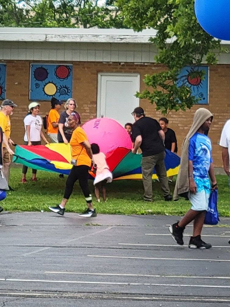 Volunteers and kids playing the rainbow parachute game at 3rd KidsFest
