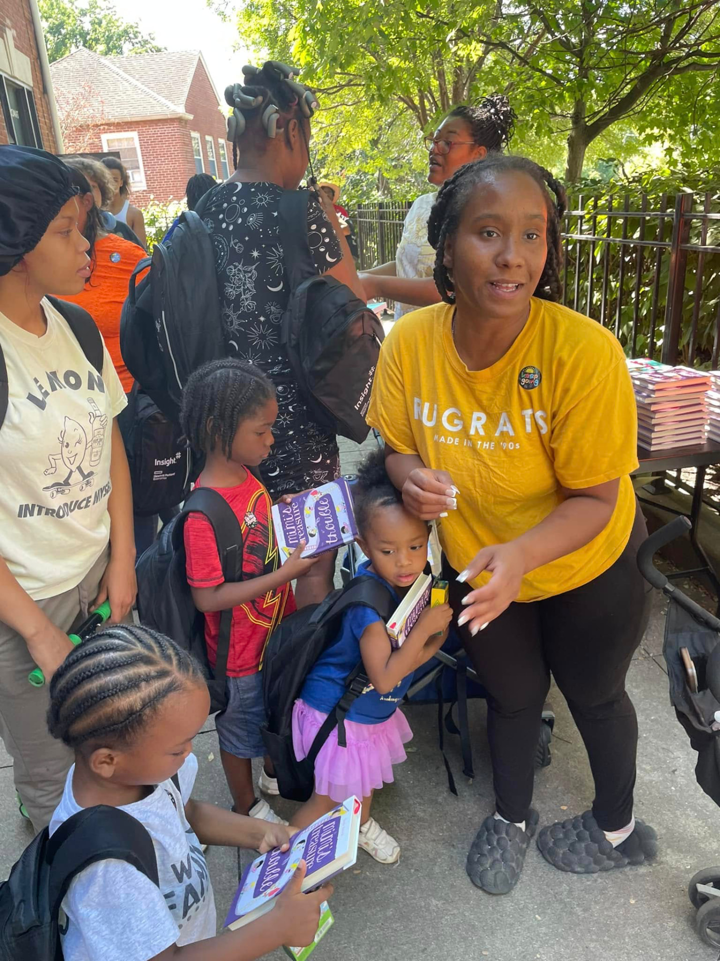 Volunteer handing out books to children with new backpacks outside at the 2024 Backpack Giveaway