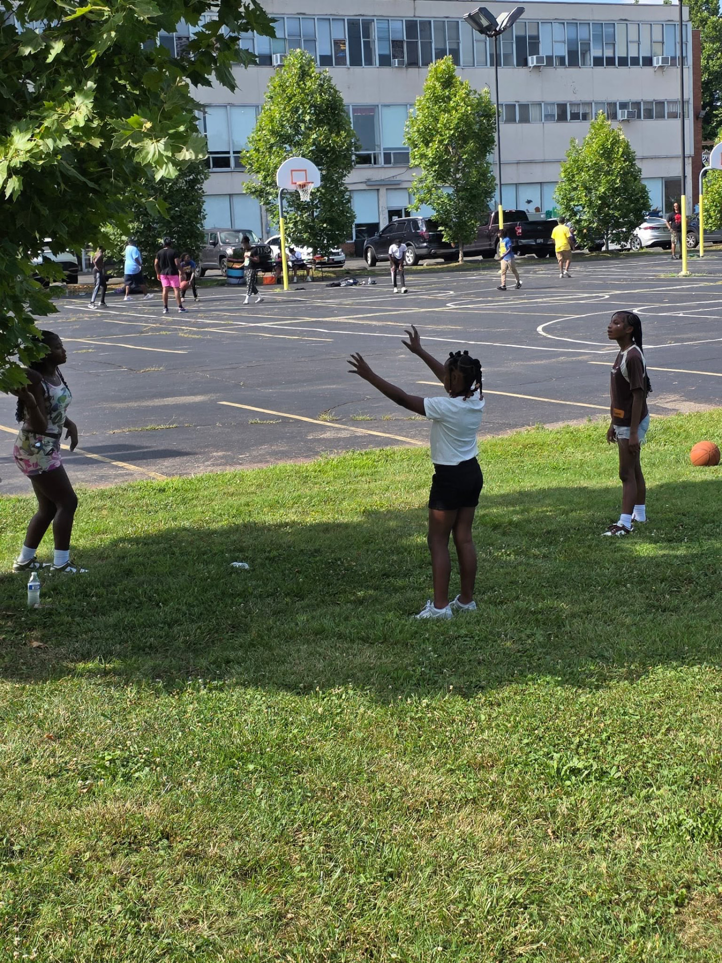 Girls passing a basketball on the grass beside the outdoor court at Saturday Hoops