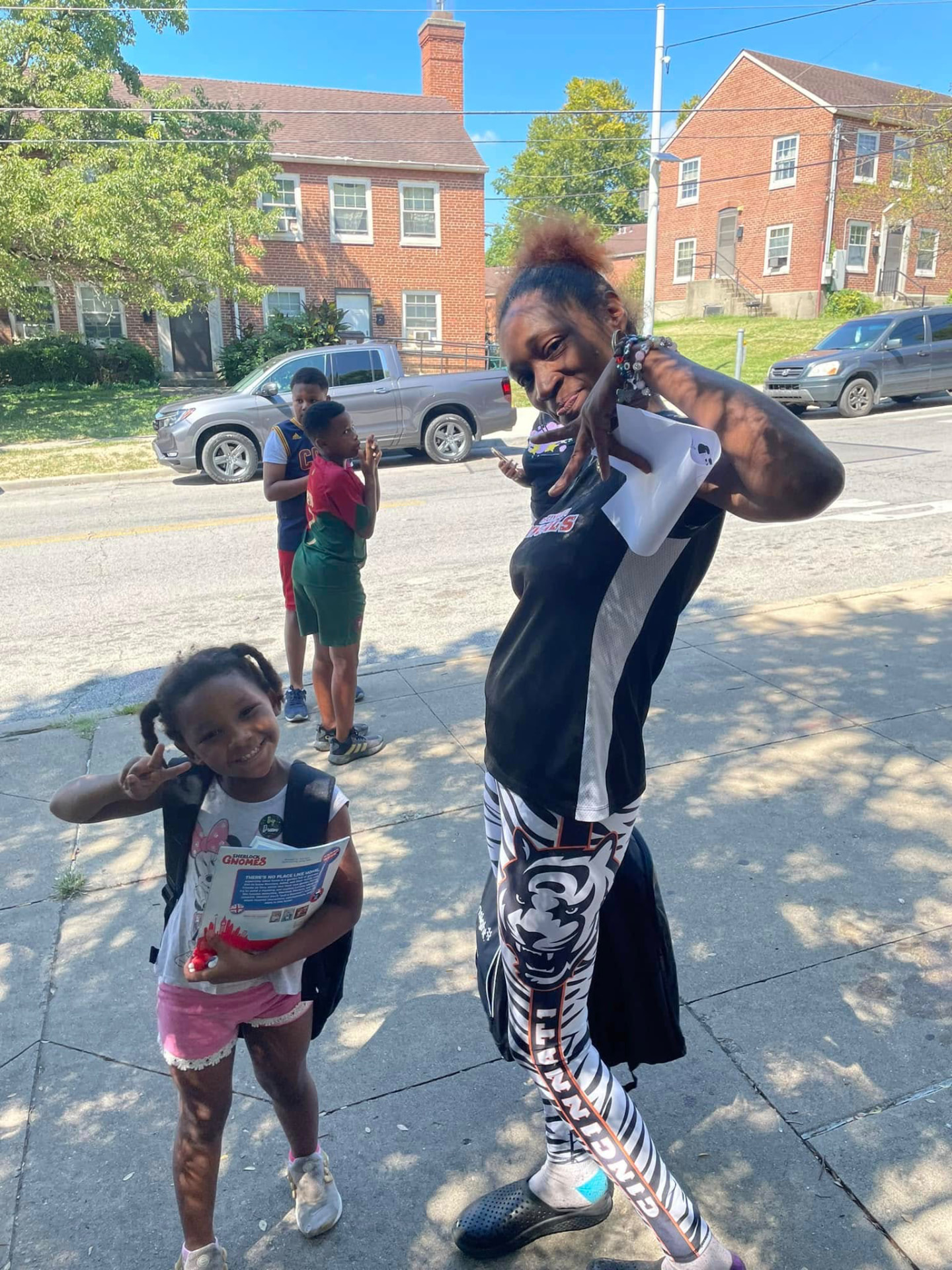 Mother and daughter posing with a new backpack and book on the sidewalk at the 2024 Backpack Giveaway