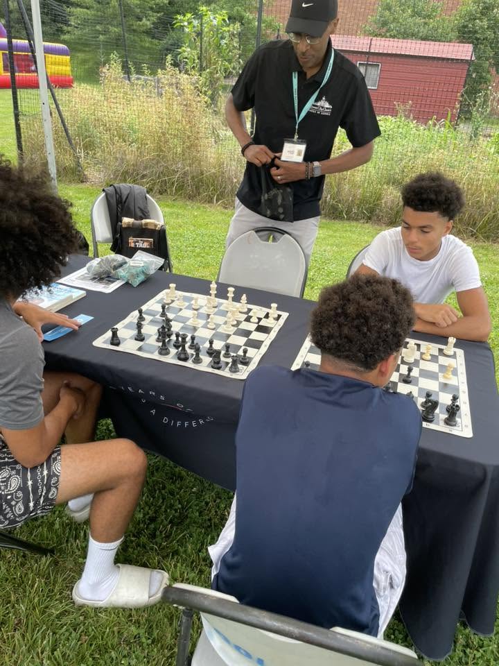 Young men playing chess outdoors with a mentor coach at 3rd KidsFest