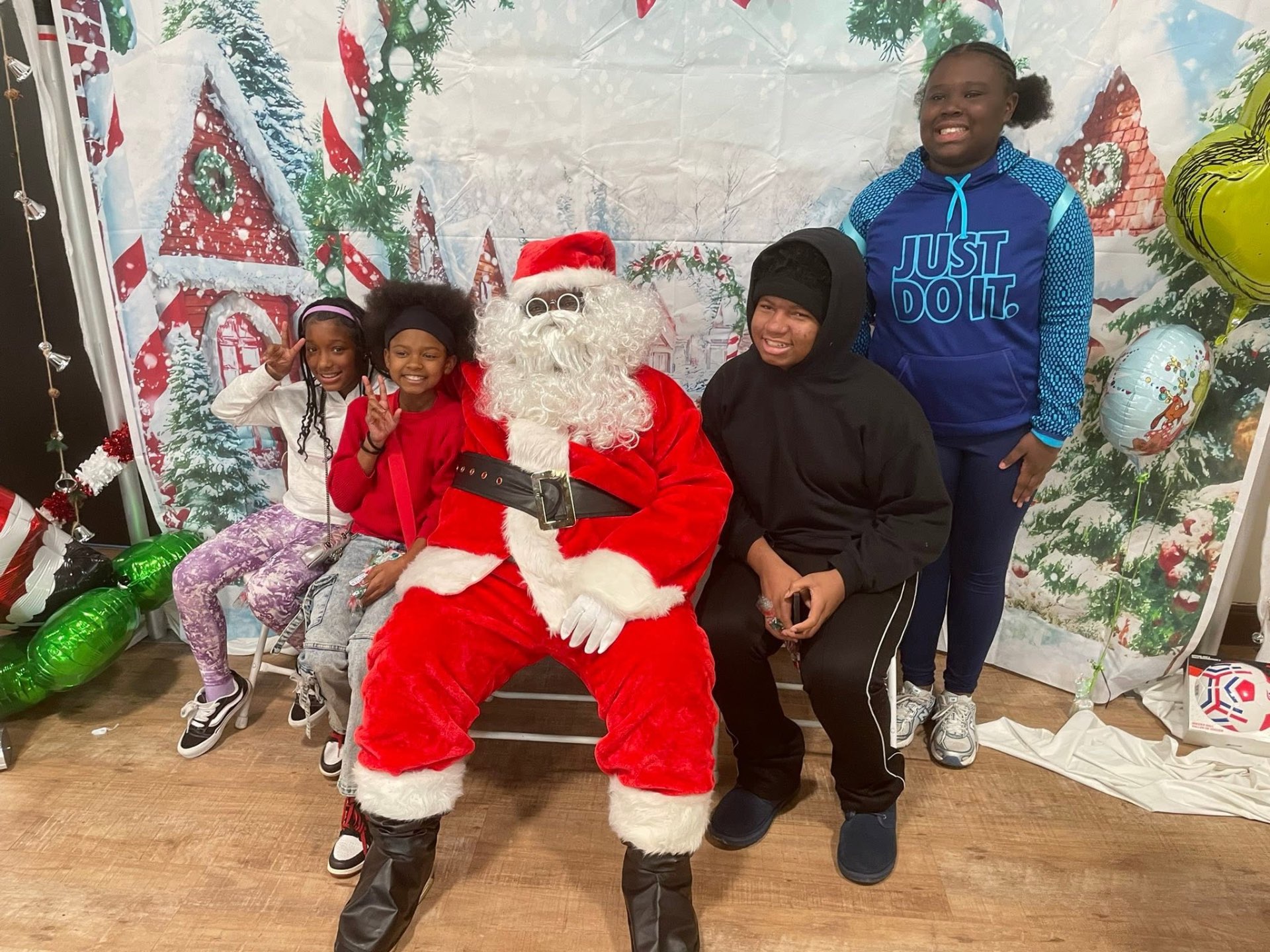 Four children posing with Santa in front of the winter village backdrop at Brothas Inc. Jingle Jam 2025