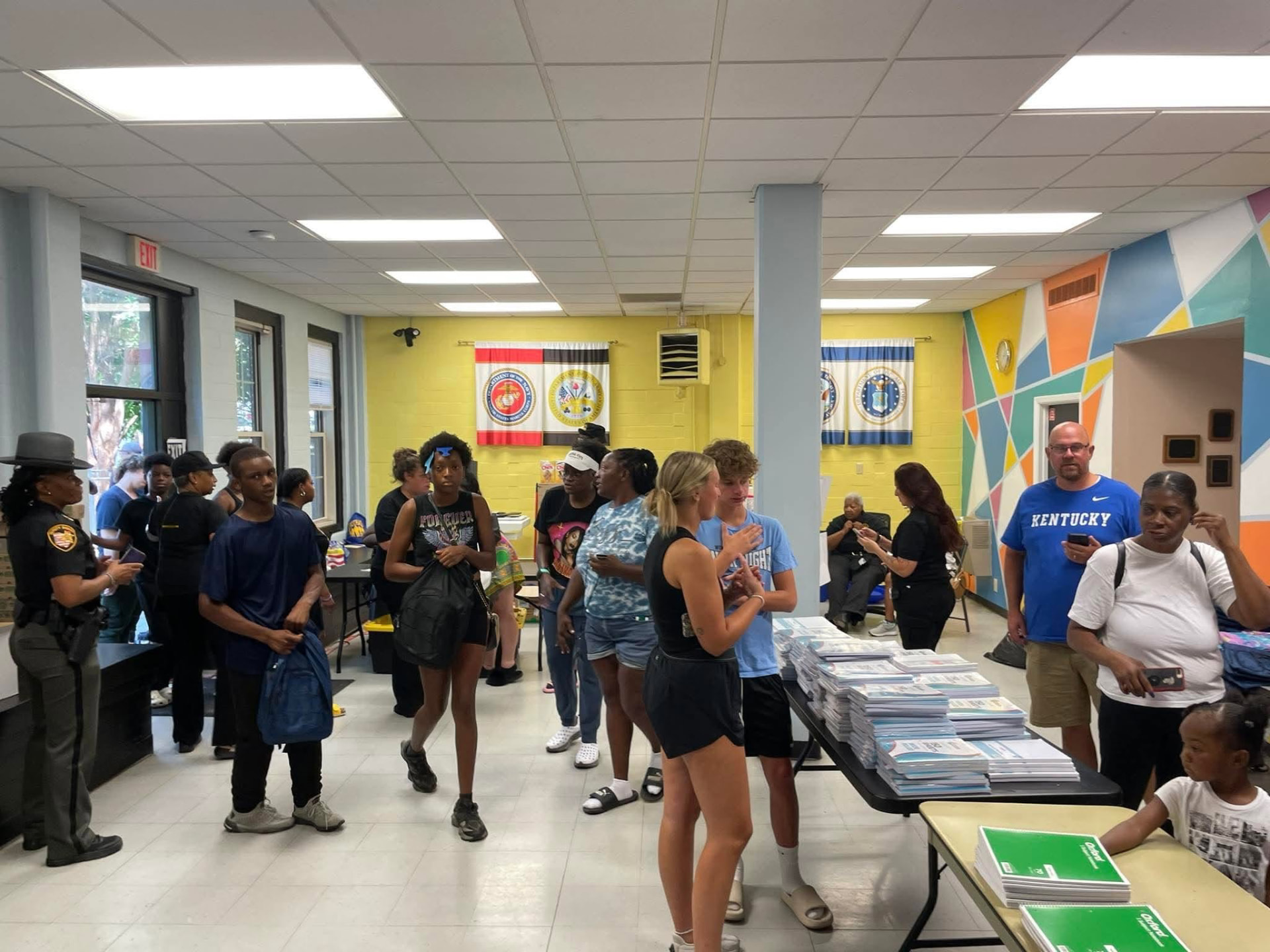 Families, teens and a sheriff's deputy filling the community room during the 2025 Backpack Giveaway