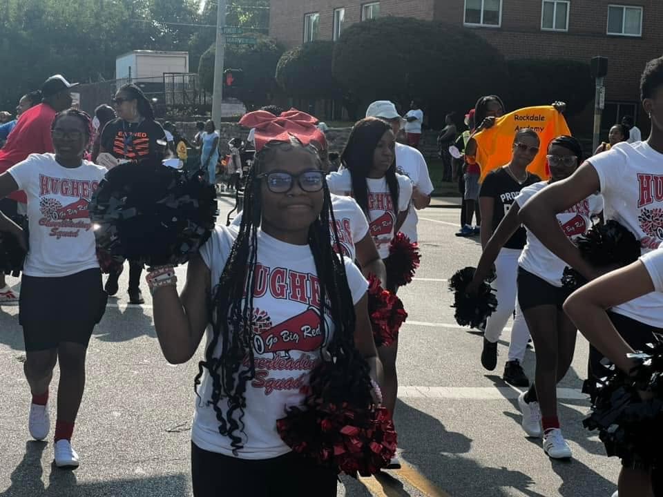 Hughes Big Red cheerleader with red bow and pom-poms marching in the Black Family Reunion Parade