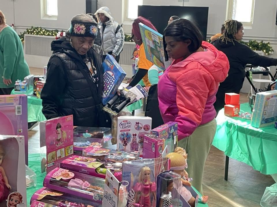 Two women browsing tables loaded with dolls, games and toys during Brothas Inc. Jingle Jam 2025