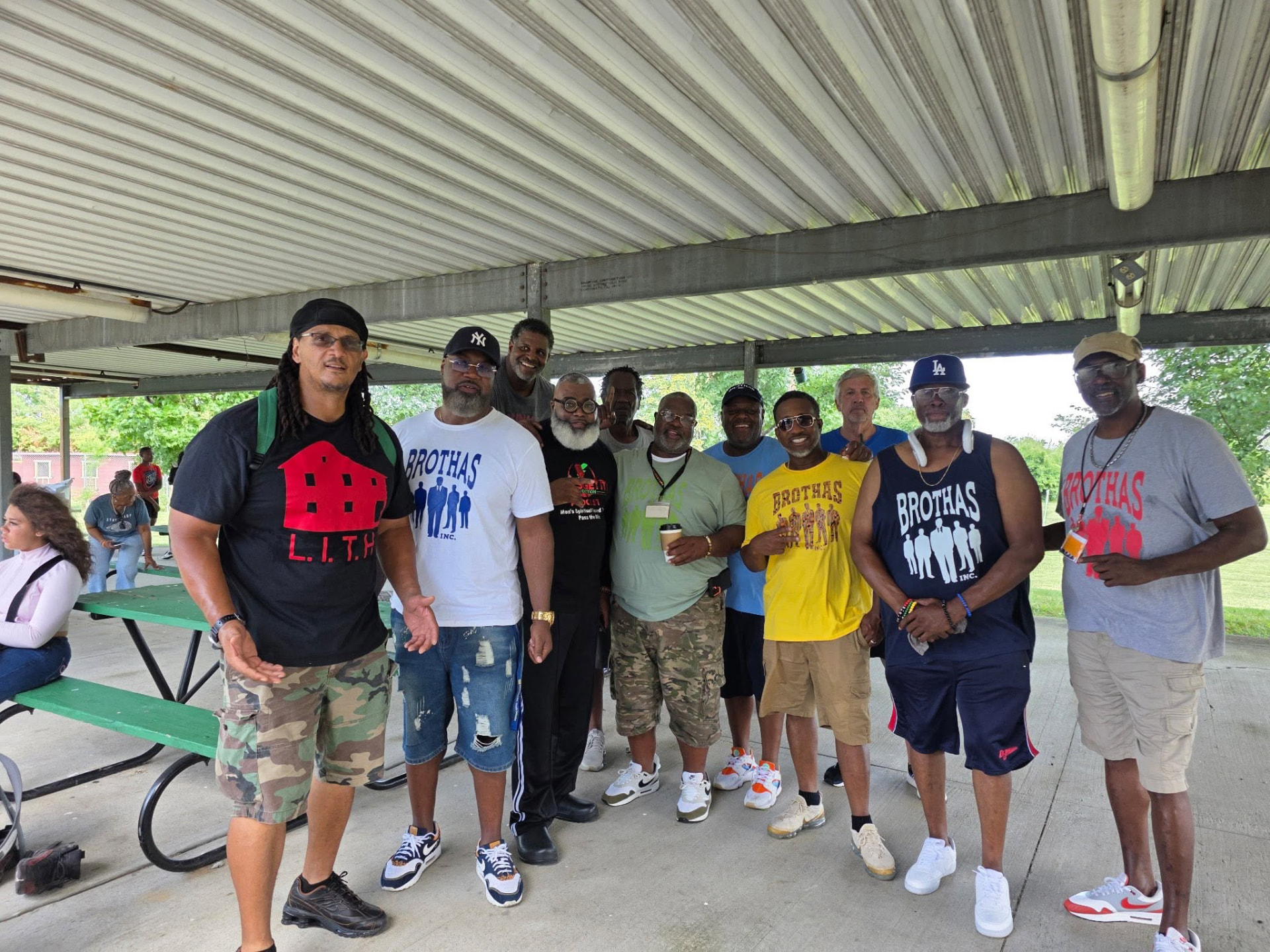 A dozen Brothas Inc. mentors in branded shirts lined up under the park shelter