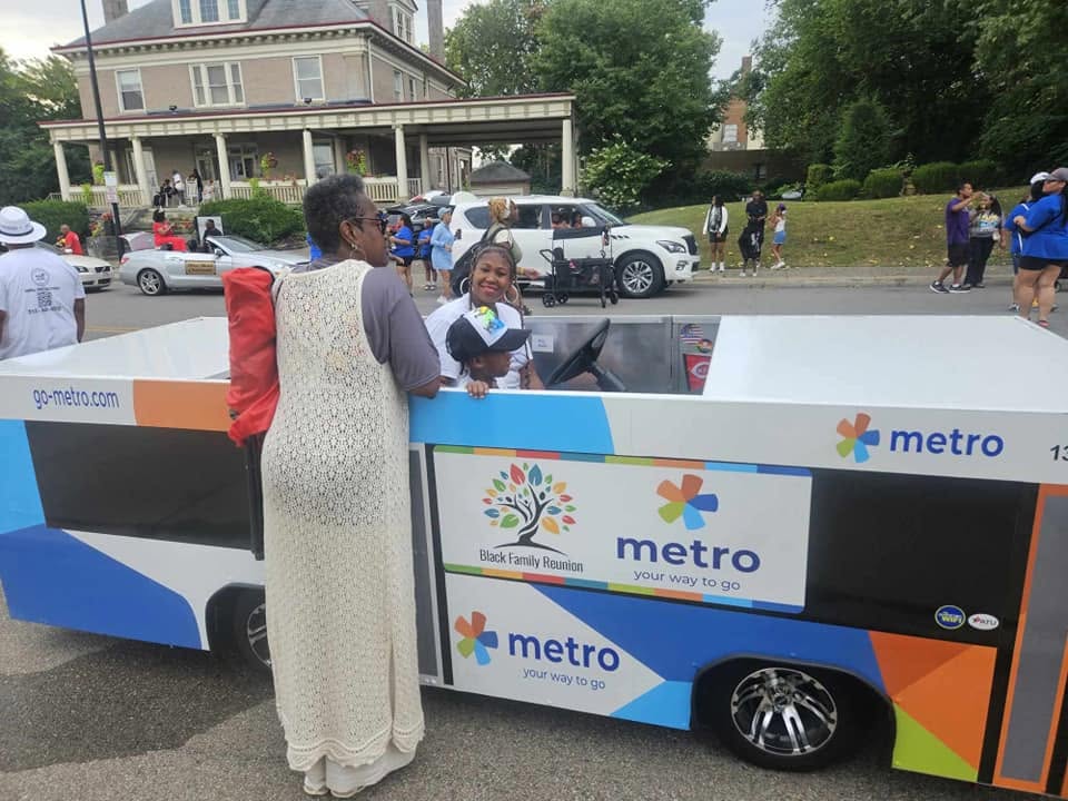 Families posing with the Cincinnati Metro Black Family Reunion parade float at the 2024 celebration